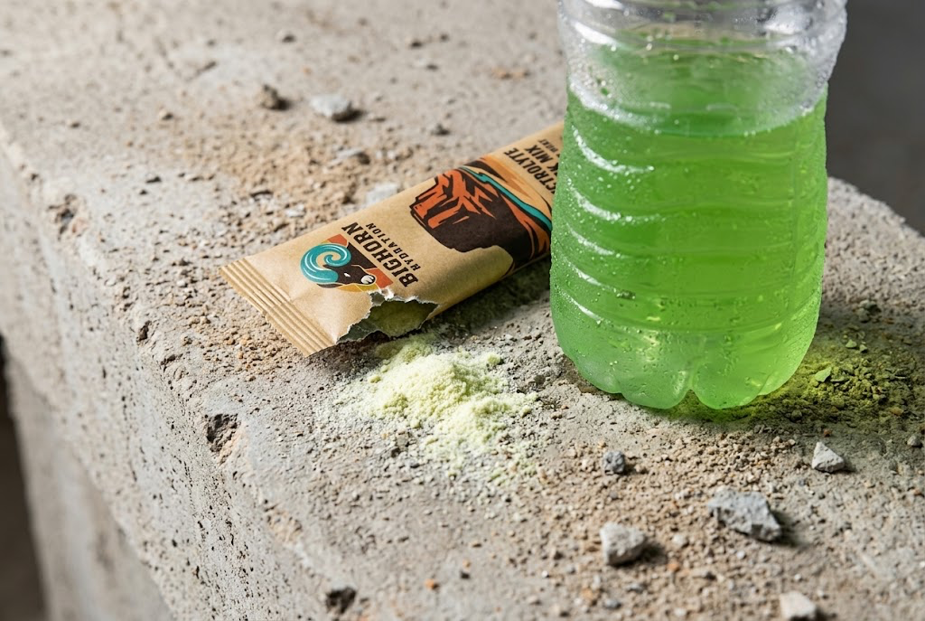 A Bighorn stick torn open on a concrete ledge, powder spilled, mixed pale green in a jobsite jar.