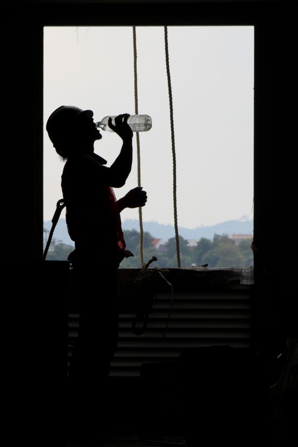 A crew member drinking on site against hard afternoon light, mid-shift.